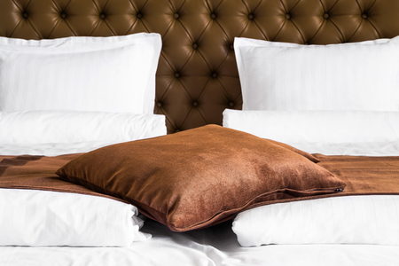 Brown cushion lying on a throw rug over a white duvet on a stylish double bed with upholstered brown headboard, close up viewの写真素材