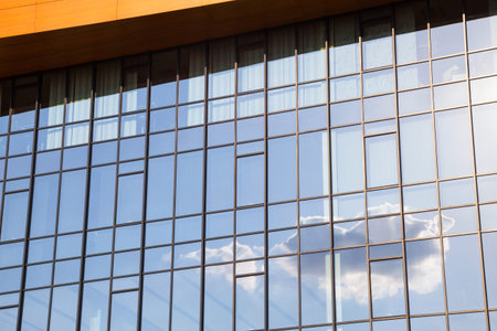 Exterior facade of a modern glass walled office block reflecting the blue sky and clouds in the...