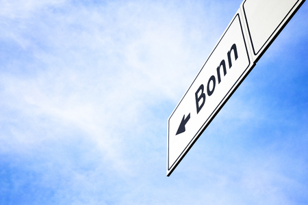 White signboard with an arrow pointing left towards Bonn, North Rhine-Westphalia, Germany, against a hazy blue sky in a concept of travel, navigation and direction. Path included for the signboardの写真素材