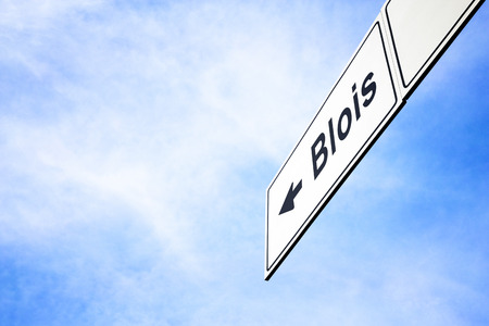 White signboard with an arrow pointing left towards Blois, France, against a hazy blue sky in a concept of travel, navigation and direction. Path included for the signboardの写真素材