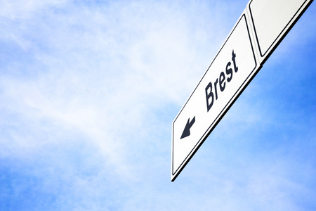 White signboard with an arrow pointing left towards Brest, France, against a hazy blue sky in a concept of travel, navigation and direction. Path included for the signboardの写真素材