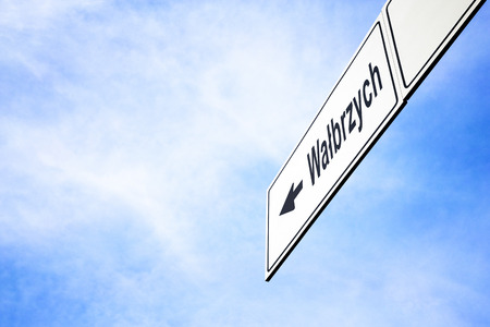 White signboard with an arrow pointing left towards Walbrzych, Poland, against a hazy blue sky in a concept of travel, navigation and direction. Path included for the signboardの写真素材