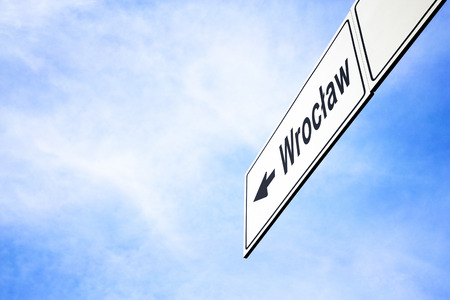 White signboard with an arrow pointing left towards Wroclaw, Poland, against a hazy blue sky in a concept of travel, navigation and direction. Path included for the signboardの写真素材