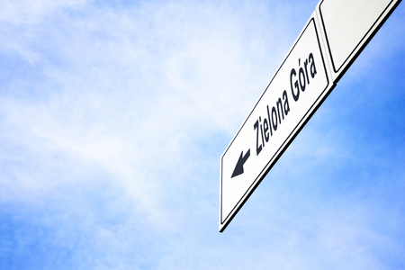 White signboard with an arrow pointing left towards Zielona Gora, Poland, against a hazy blue sky in a concept of travel, navigation and direction. Path included for the signboardの写真素材