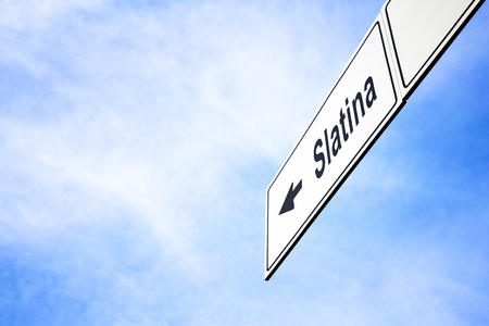 White signboard with an arrow pointing left towards Slatina, Romania, against a hazy blue sky in a concept of travel, navigation and direction. Path included for the signboardの写真素材
