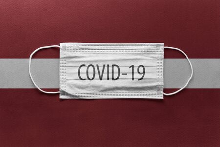 An individual face medical surgical mask on Latvia national flag Background. Health mask. Protection against COVID-19 virus, influenza, SARS. Save Latvia from Coronavirusの写真素材