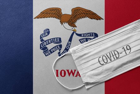Face Medical Surgical White Mask with COVID-19 inscription lying on Iowa State Flag. Coronavirus in Iowaの写真素材