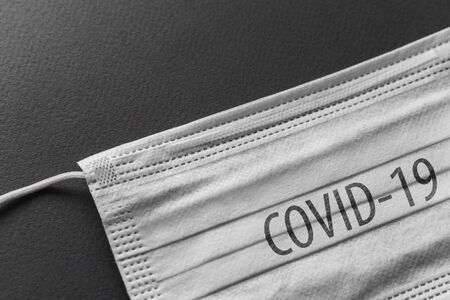 White surgical medical face mask with COVID-19 inscription, protection against coronavirus on black background.の写真素材