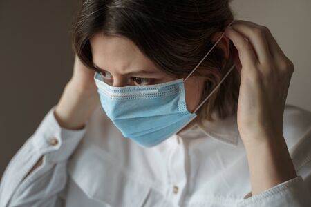 Young woman putting on blue protective medical face mask. Protection from Coronavirus, covid-19の写真素材