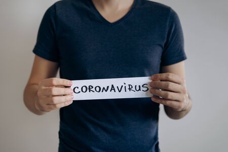 Man in blue t-shirt holds sheet with the word Coronavirus. Pandemic of COVID-19. Coronavirus quarantine isolation concept. Stay at home. Close-up shot.の写真素材
