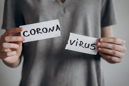 Victory against coronavirus quarantine concept. Young woman in grey t-shirt tears the paper with the word Coronavirus. Pandemic of COVID-19 is over. Finish of isolaion. Close up shot.の写真素材