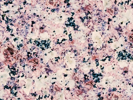 A close-up of a surface of treated rose granite rock plate. A fragment of a stone wall decoration. Texture of bright rose granite facing material.の写真素材