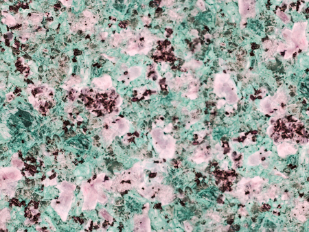 A close-up of a surface of treated rose and green granite rock plate. A fragment of a stone wall decoration. Texture of red granite facing material.の写真素材