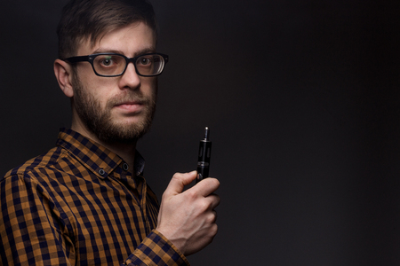 man with a beard wearing glasses on black background smoke Vape. large portrait of man. electronic cigarette. E-cigarette for vaping. Popular devices of the year - modern device. Stop smokingの写真素材