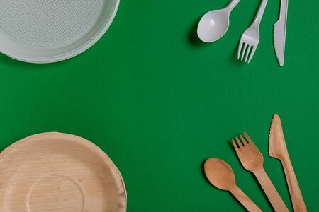 From above plastic utensils versus ecological lumber forks and knives against freen background.の写真素材