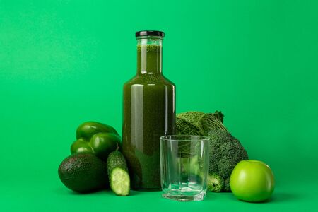 Bottle and empty glass with green natural freshly squeezed vegetable juice smoothie with ingredients isolated on green background. Detox diet is good for low-calorie foods. Healthy eating concept.の写真素材