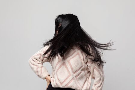 Portrait of a beautiful young woman with flying hair. A young attractive brunette shakes her head on a light gray background, wearing a warm white sweater.の写真素材