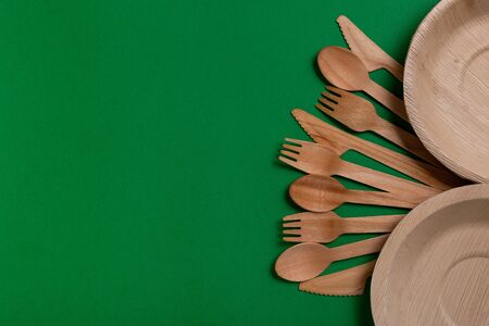 Eco-friendly disposable utensils made of bamboo wood on a green background. Draped spoons, fork, knives, bamboo bowls with.の写真素材