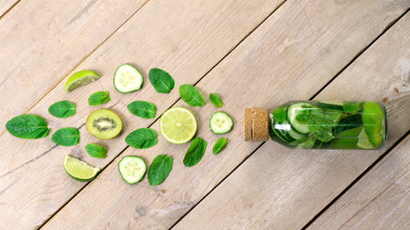 Water bottle with lime and mint on wooden table. Infused water with lemon, cucumber and mint on...