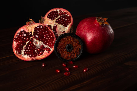 A hookah smoking bowl filled with red pomegranate flavor tobacco lies next to a whole and cut...