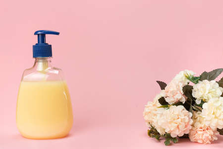 Yellow liquid soap bottle and beautiful delicate flowers on a pink background. Clean hands concept. Shampoo, Liquid Soap, Aromatic Bath Salt And Other Toiletry.の写真素材