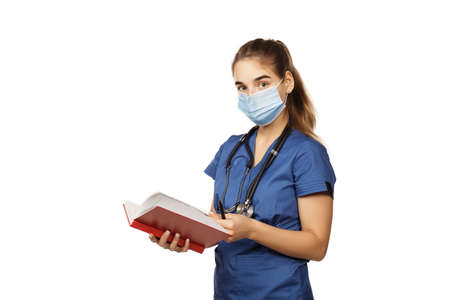 Young beautiful woman doctor in blue surgical gown with stethoscope and red notebook writes anamnesis isolated on white background. Copspaceの写真素材