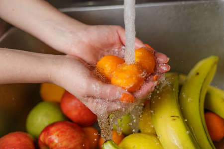Happy woman washing fruit at kitchen. bananas, tangerines, applesの写真素材