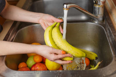 Happy woman washing fruit at kitchen. bananas, tangerines, applesの写真素材