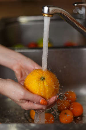 Happy woman washing fruit at kitchen. bananas, tangerines, applesの写真素材