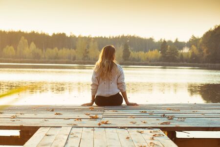 A young slender blonde sits on a wooden pier with her back.の写真素材