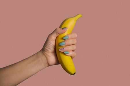 Female hand with creative manicure in pastel colors holds a yellow bananaの写真素材