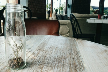 Coffee beans and dried flowers in a glass bottle on wooden table in caf