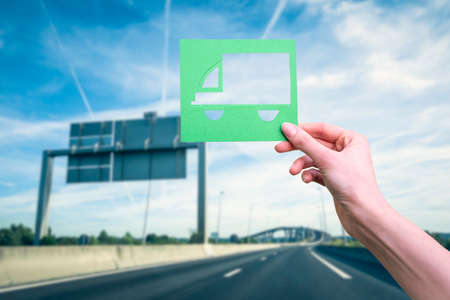 Hand holds green logistics symbol against highwayの写真素材