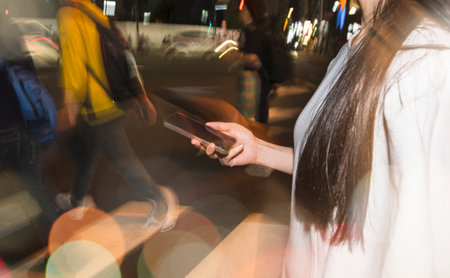 Woman using smartphone on busy city street at nightの写真素材