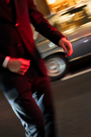 Blurred man in red light near parked classic car at nightの写真素材