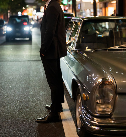 Businessman standing beside classic car on city street at night