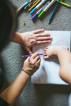 Parent tracing baby foot on notebook with colored pencils