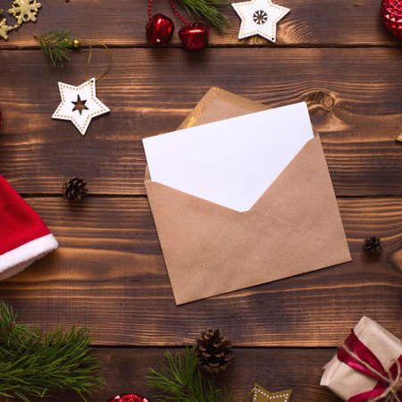 Mail envelope made of craft paper with a white sheet for text on a wooden background with Christmas decor. A letter to Santa Claus, a wish list, a new year's dream, a gift. Flat lay, copy spaceの写真素材