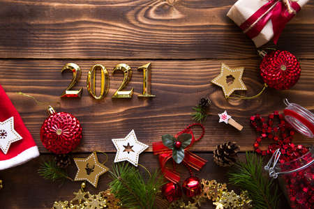 Christmas flat lay with new year 2021 symbol of gold numbers in the center. Holiday atmosphere, wooden stars, toys, beads, red balls, spruce branches on a dark background. Space for textの写真素材