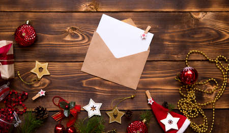 Mail envelope made of craft paper with a white sheet for text on a wooden background with Christmas decor. A letter to Santa Claus, a wish list, a new year's dream, a gift. Flat lay, copy spaceの写真素材
