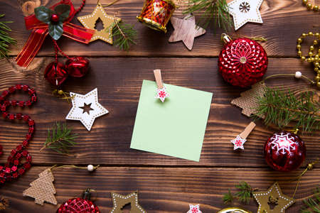 Christmas flat lay of red balloons and wooden stars and clothespins on a dark background with a square sheet for notes in the center. New year's frame, space for text. Xmas toys, beads, pine branchesの写真素材