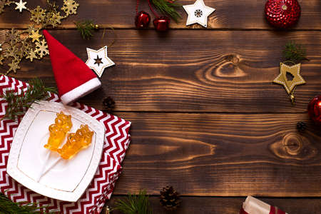 Two lollipops on stick in shape of symbol new year 2021 - bull on white saucer, towel with ornaments and Christmas decor on wooden background. Jewelry stars, beads, ball, fir. Flat lay, copy spaceの写真素材