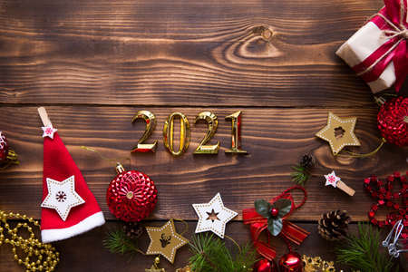 Christmas flat lay with new year 2021 symbol of gold numbers in the center. Holiday atmosphere, wooden stars, toys, beads, red balls, spruce branches on a dark background. Space for textの写真素材