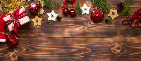 Frame with Christmas decor on a wooden background. New year, holiday atmosphere, green spruce branches, decorations: stars, gift box, beads, ball, bells, cones. Space for text, flat layの写真素材