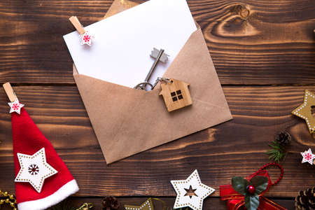 Christmas flat lay on a wooden background with keys to new house in the center with a envelope with a note sheet. New year, transfer, shares of the mortgage, the rental of a cottage. Space for textの写真素材