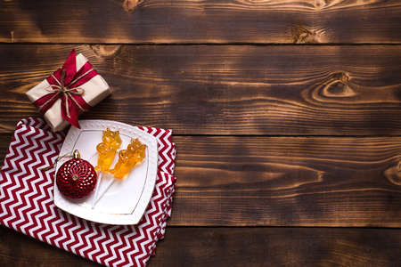 Two lollipops on stick in shape of symbol new year 2021 - bull on white saucer, towel with ornaments and Christmas decor on wooden background. Jewelry stars, beads, ball, fir. Flat lay, copy spaceの写真素材