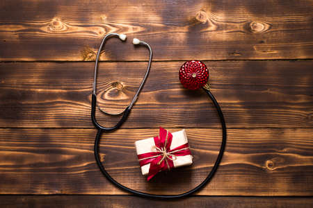 Christmas flat lay on a medical theme. Decorations for the new year from stars, ball, ribbons, Santa hats, and a doctor's stethoscope. Wooden background, space for textの写真素材