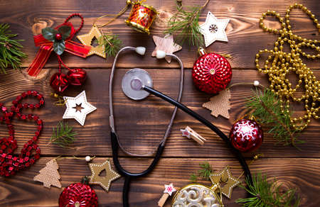 Christmas flat lay on a medical theme. Decorations for the new year from stars, ball, ribbons, Santa hats, and a doctor's stethoscope. Wooden background, space for textの写真素材