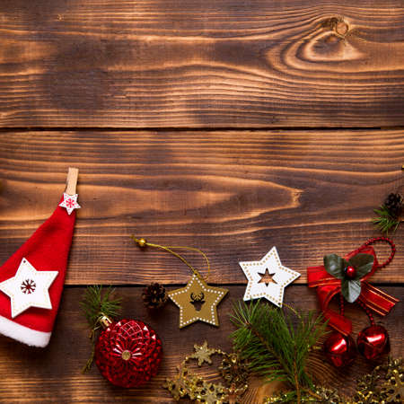 Frame with Christmas decor on a wooden background. New year, holiday atmosphere, green spruce branches, decorations: stars, gift box, beads, ball, bells, cones. Space for text, flat layの写真素材