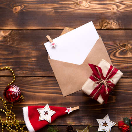 Mail envelope made of craft paper with a white sheet for text on a wooden background with Christmas decor. A letter to Santa Claus, a wish list, a new year's dream, a gift. Flat lay, copy spaceの写真素材